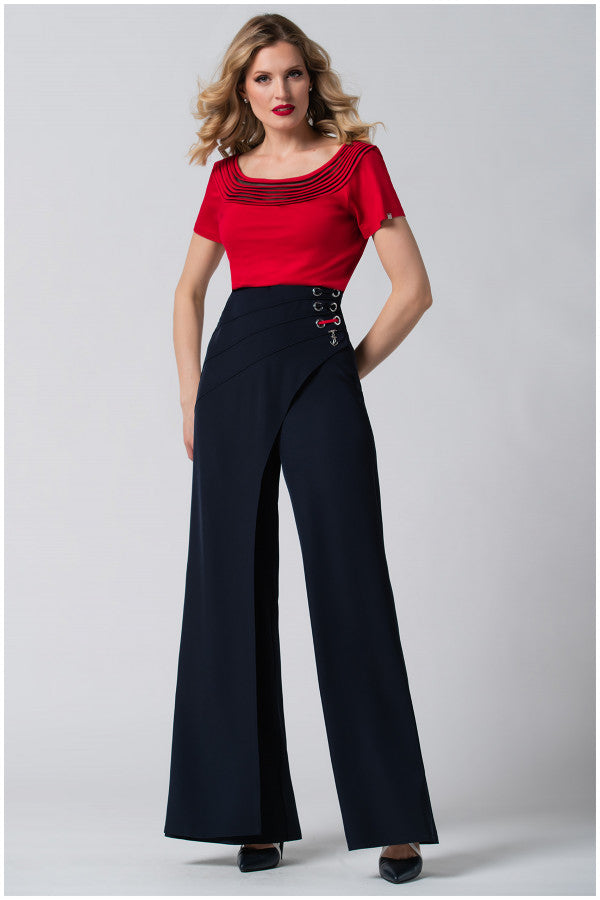Woman with wavy blonde hair wearing a red top and high-waisted wide-leg navy pants against a gray background.