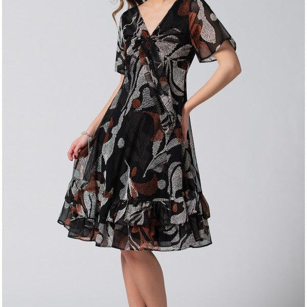 Woman wearing a flowing wide dress black and brown patterned Short Dress Lola with deep V-neck and soft flounces, styled with black heels.