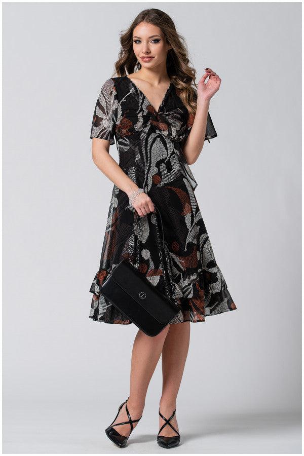 Woman wearing a flowing boho short dress with flounces and a deep V-neckline, holding a black handbag and wearing heels