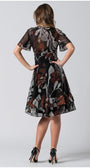 Woman wearing a black and brown patterned short wide dress with flounces, standing with hands on hips, back view.