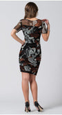 Woman wearing a fitted floral patterned short dress with sheer sleeves and high heels, posing with her back to the camera.