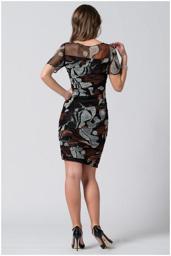 Woman wearing a fitted floral patterned short dress with sheer sleeves and high heels, posing with her back to the camera.