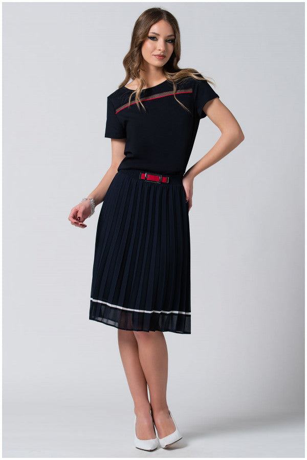 Woman wearing navy pleated midi skirt with white accents and a red buckle belt paired with black top and white heels