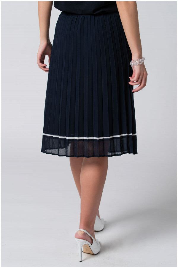Woman wearing navy blue pleated midi skirt with white trim, paired with white high heels, shown from behind