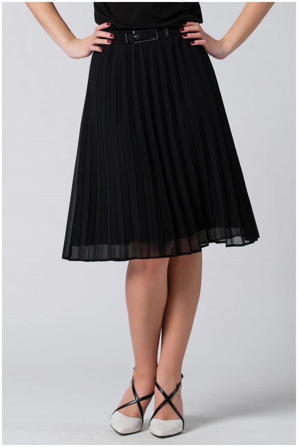 Black pleated skirt with stretch waistband and decorative buckle, styled with black top and white heels.