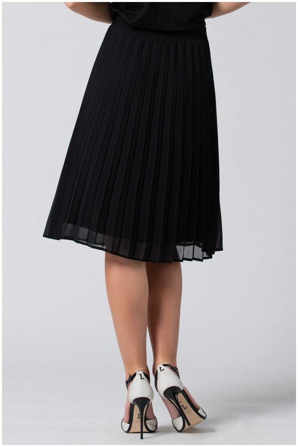 Woman wearing a black pleated skirt with a sheer hem and white high heels with black straps