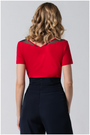 Person wearing a red top with black trim and navy pants on a gray background