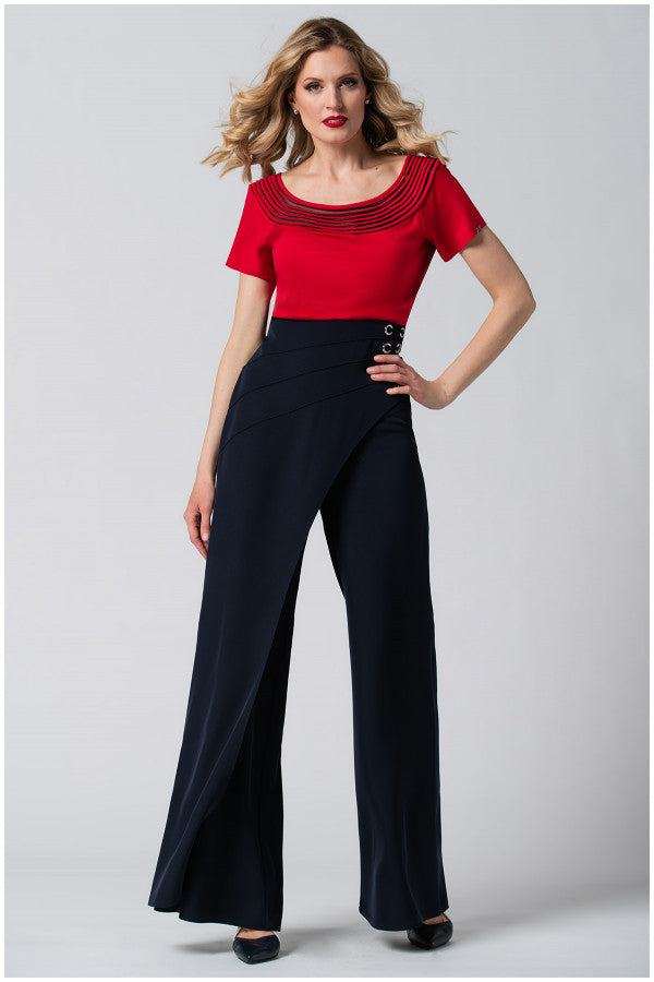 Woman wearing a red office elegant blouse Lola Top with pleated neckline and high-waisted black wide-leg trousers posing against a grey background