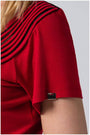 Close-up of red office elegant blouse short sleeve with pleated neckline detail and small metal logo tag on soft viscose blend fabric.