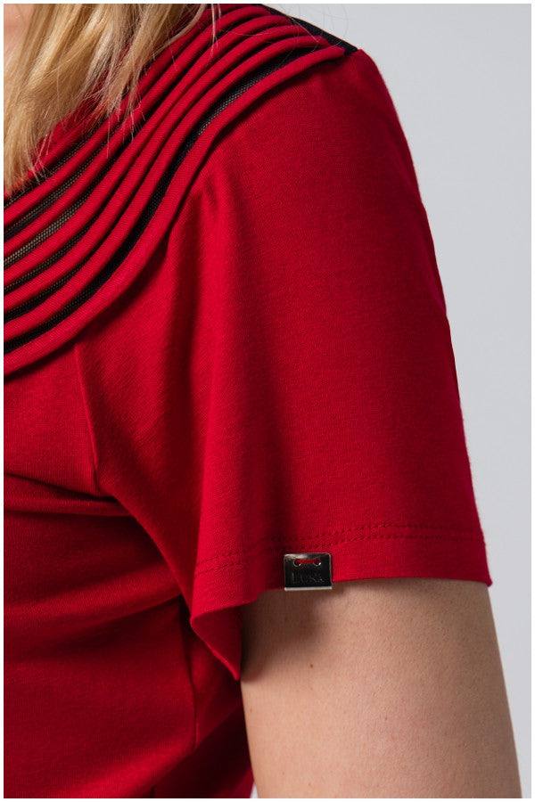 Close-up of red office elegant blouse short sleeve with pleated neckline detail and small metal logo tag on soft viscose blend fabric.