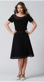 Woman wearing a black Lola business Top in Black with pleated neckline and short sleeves paired with a black pleated skirt and white shoes.