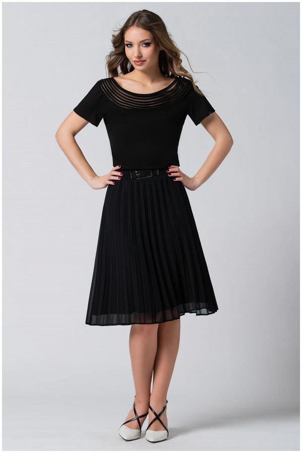 Woman wearing a black Lola business Top in Black with pleated neckline and short sleeves paired with a black pleated skirt and white shoes.