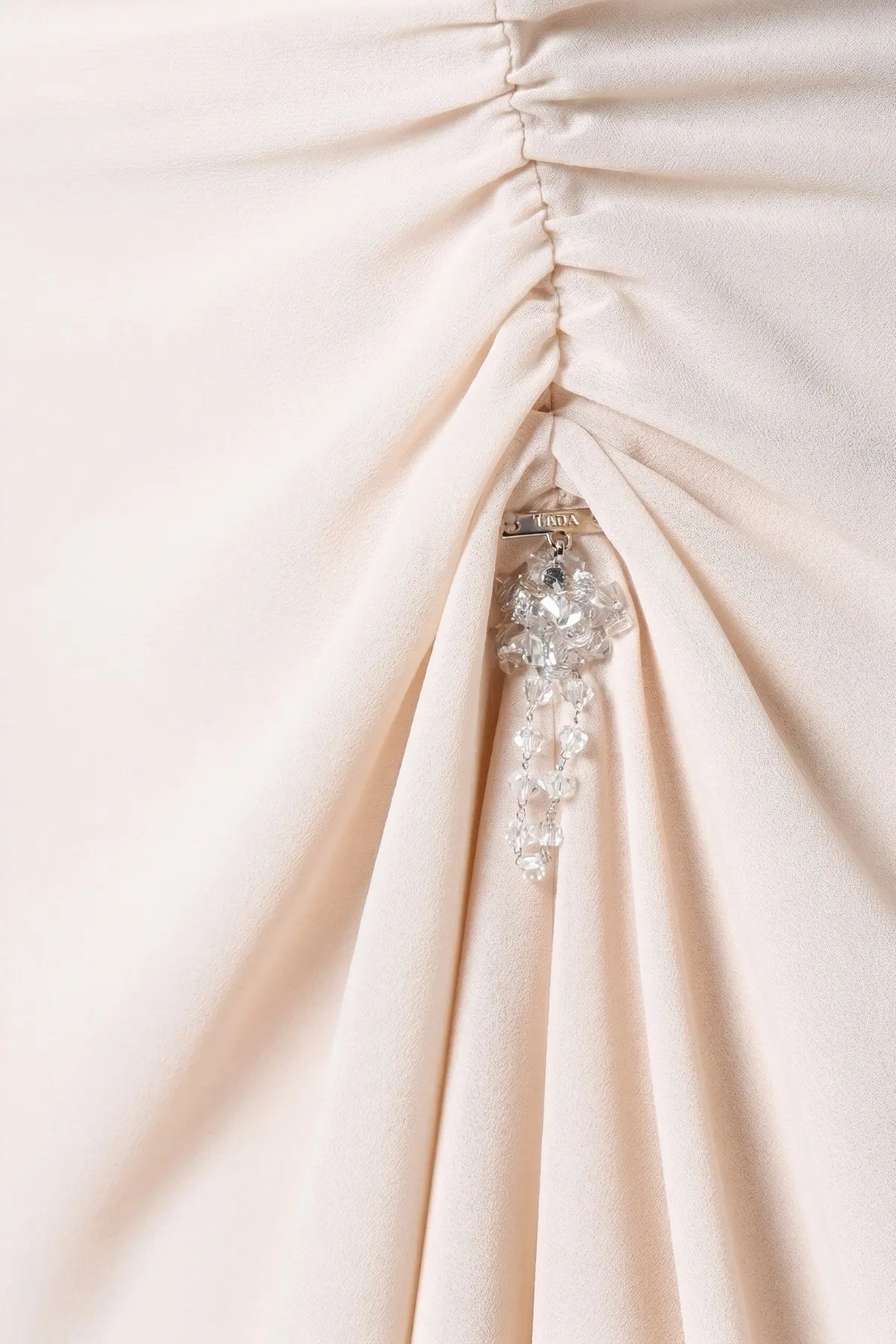Side-gathered ruching at the right hip with hanging crystal cluster drop on pale beige polyester crepe