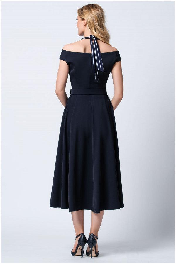 Woman wearing navy off-shoulder elegant midi dress with halter tie and high heels, standing against white background