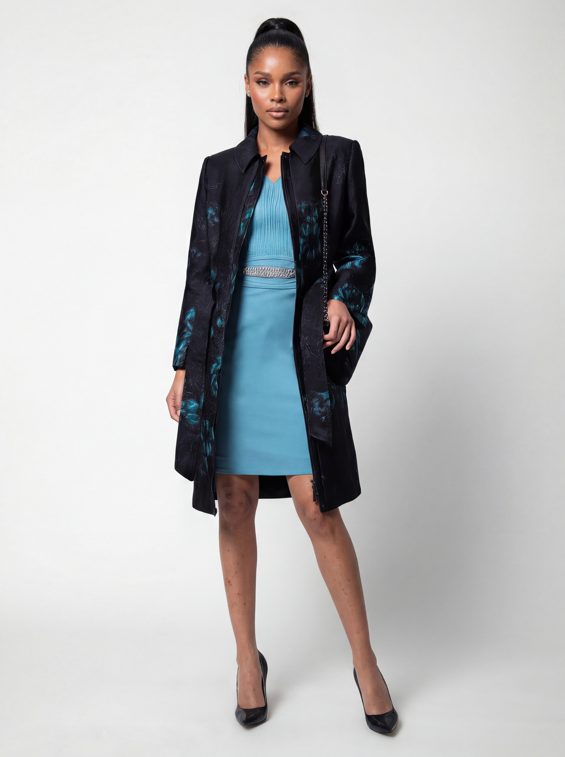 Woman wearing a long black coat with floral patterns over a blue dress on a white background