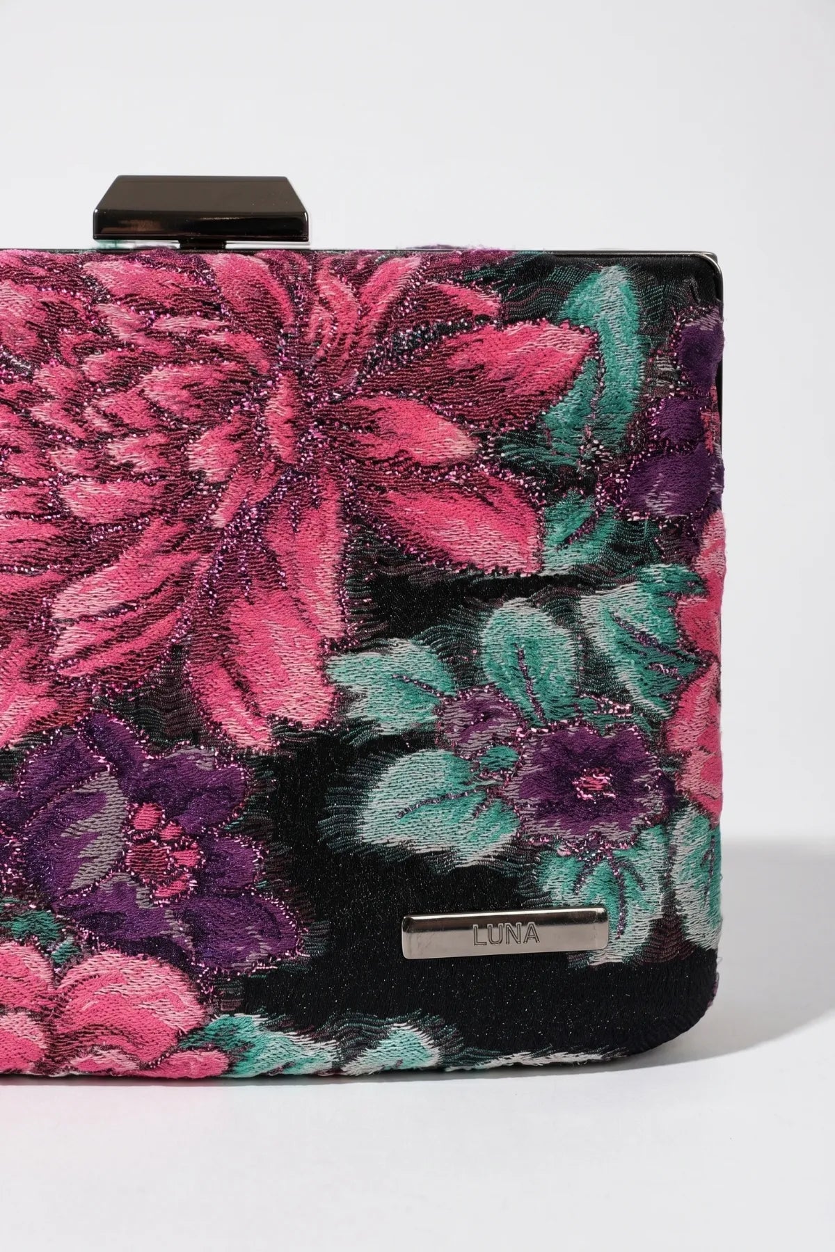 Close-up of Regina floral clutch showing the floral textile, Luna logo plate, and top clasp detail.