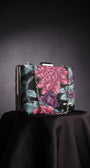 Regina floral clutch in cyclamen, purple, and teal on a dark surface with a detachable chain strap.
