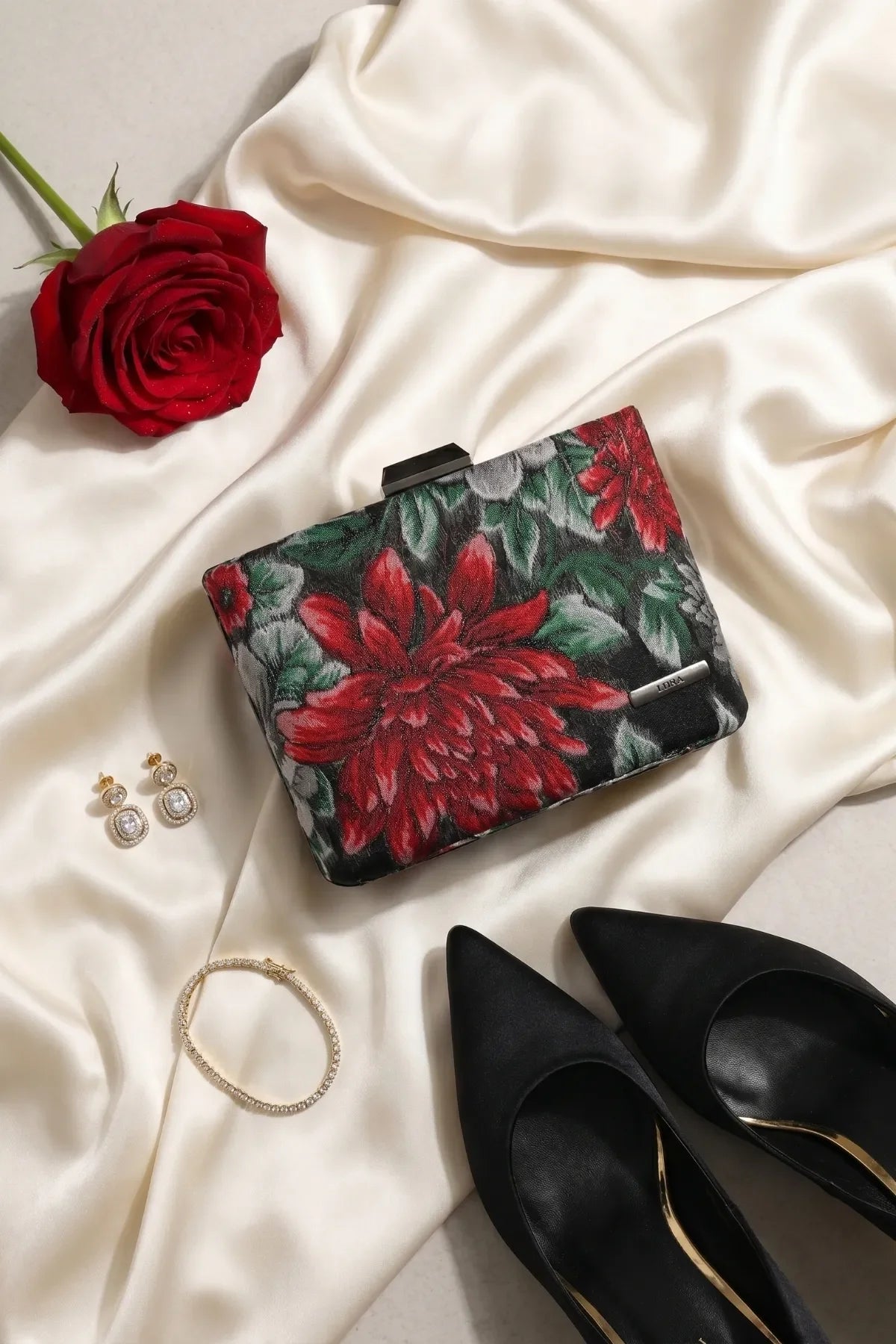 Regina floral clutch styled on cream satin with black heels, jewelry, and a red rose.
