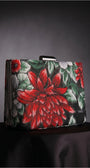 Regina red floral clutch on a dark draped surface highlighting the red floral motif and structured shape.