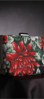 Regina red floral clutch on a dark draped surface highlighting the red floral motif and structured shape.
