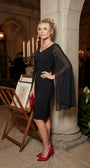 Rebeka black cape-sleeve dress worn at an evening event styled with red accessories