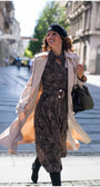 Woman walking confidently on city street wearing Kim Classic Long Coat in Beige over patterned dress and black beret
