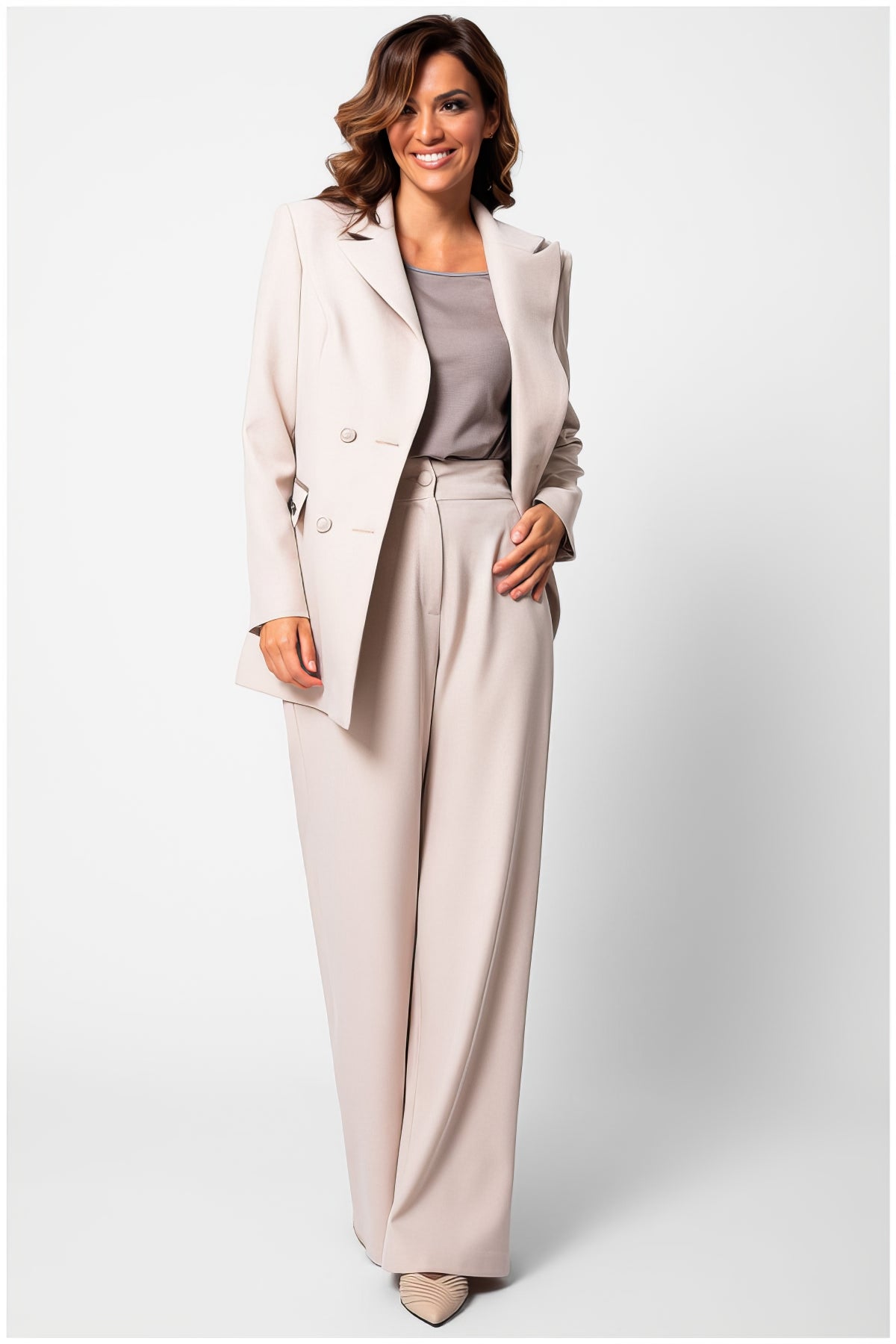 Woman wearing Natasha Wide Leg Trousers in Sand Beige styled with matching blazer and taupe top in a studio setting