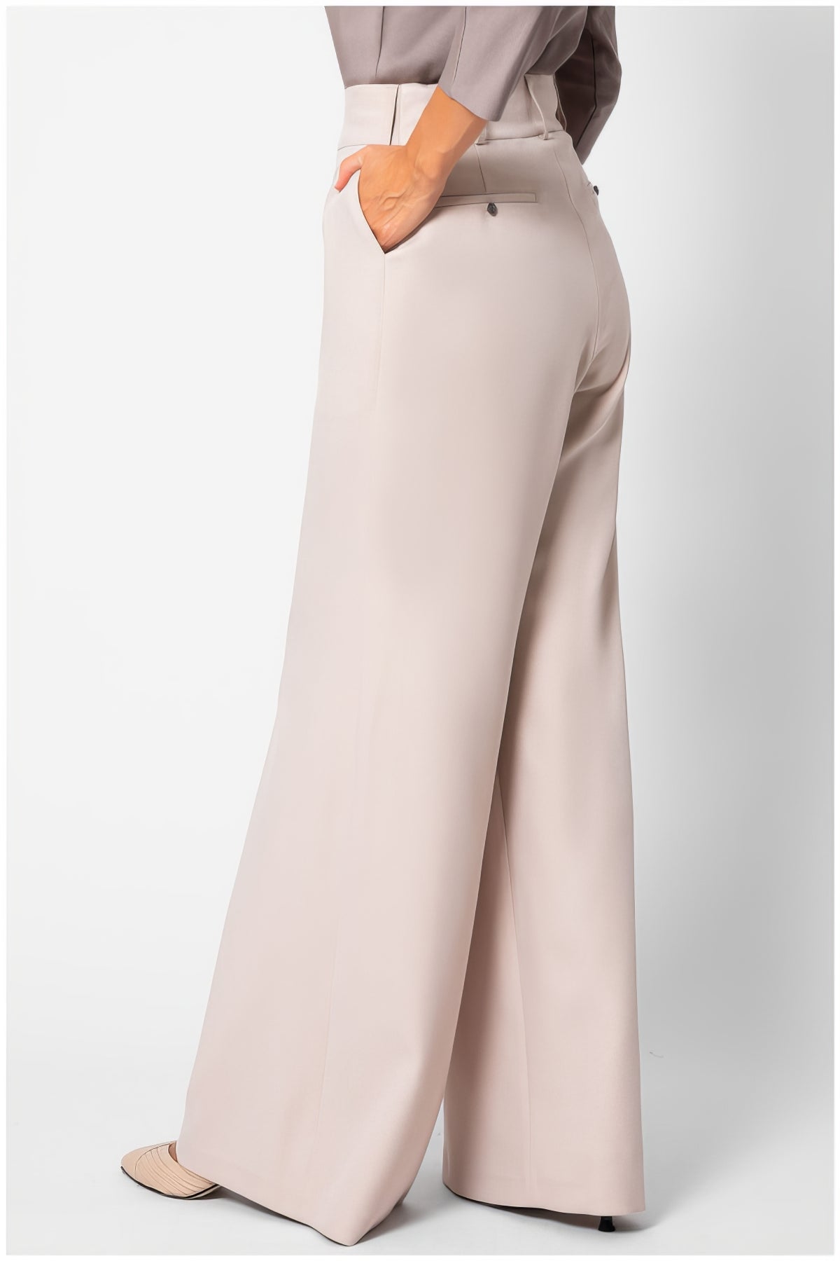 Back view of Natasha Wide Leg Trousers in Sand Beige showing smooth fabric and wide-leg silhouette with hand in pocket.