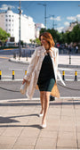 Woman walking on city street wearing Rea Jacquard Trench Coat in Beige over black dress with heels and clutch bag.
