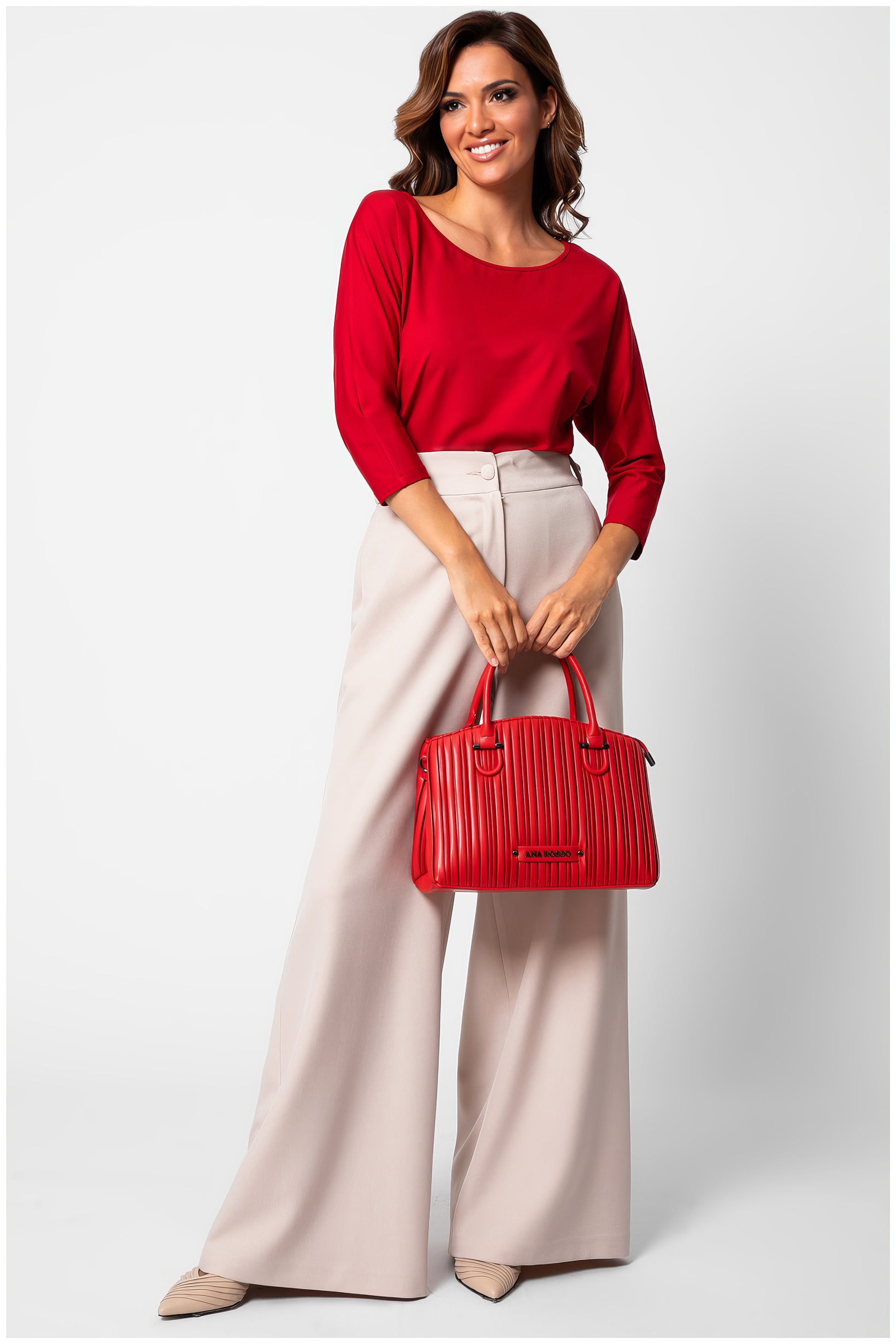 Woman wearing Eva Classic Top in Scarlet Red with beige high-waist wide-leg pants holding a red handbag