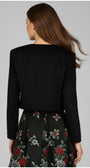 Back view of a woman wearing the Frida Cropped Zip Blazer in Black with a floral skirt against a gray background