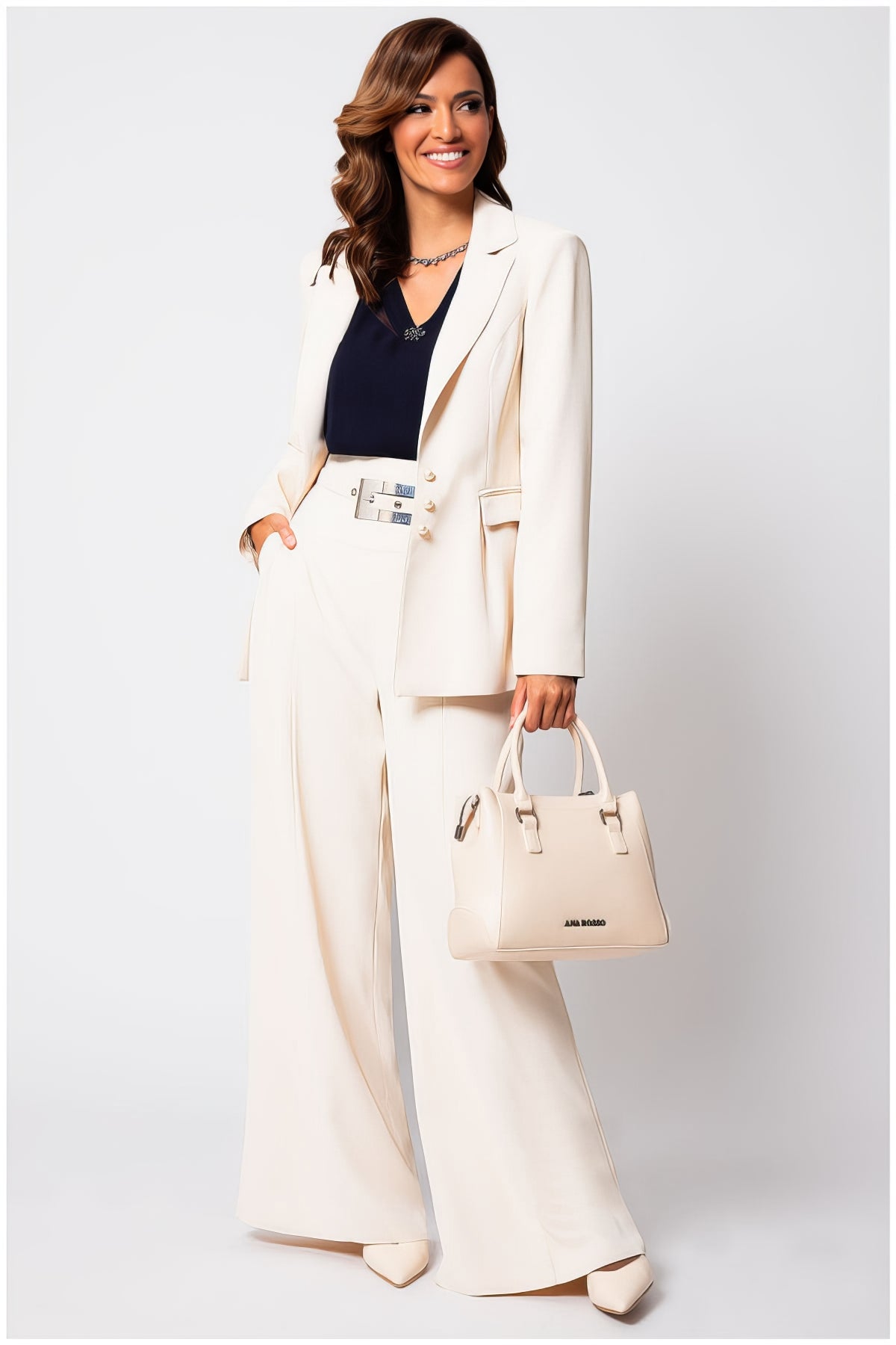 Woman wearing the Agatha Pearl Detail Blazer in Ivory with matching wide-leg pants and a stylish handbag