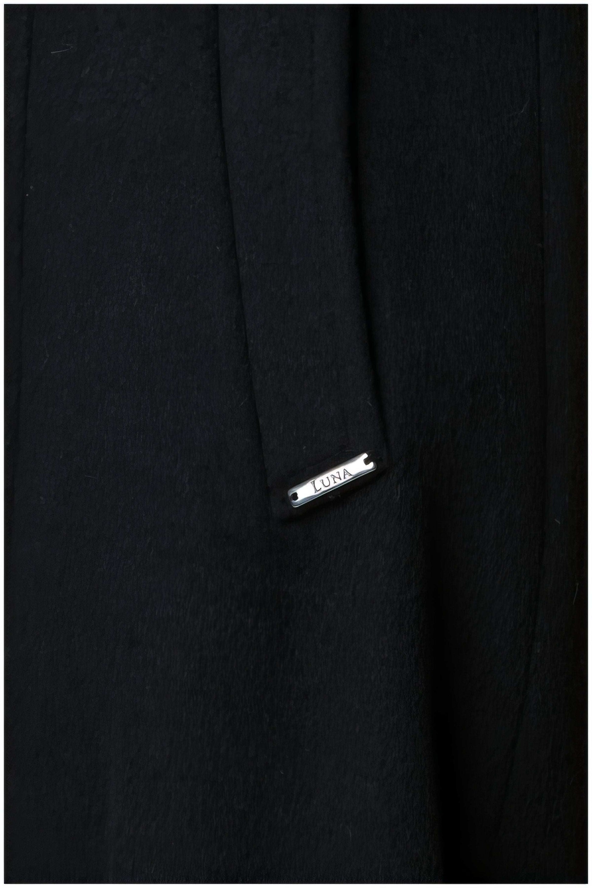 Close-up detail of Nicole Wool Wrap Coat in Solid Black featuring Luna brand metal tag on wool fabric