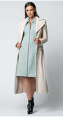 Woman wearing the Linea Belted Midi Coat in Ivory styled with a light blue dress and black ankle boots on white background