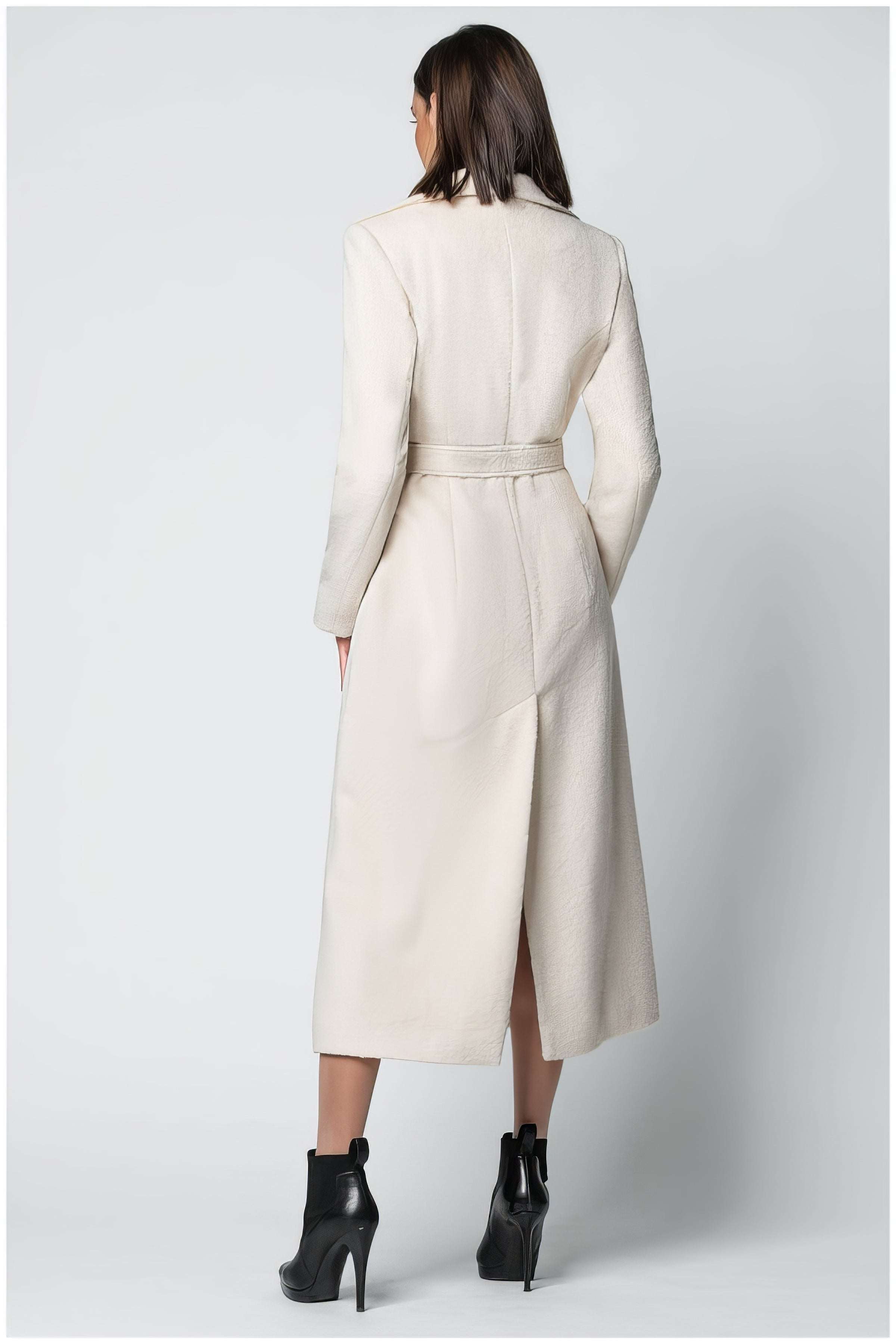 Woman wearing Linea Belted Midi Coat in Ivory with a belted waist and midi length styling from the back view