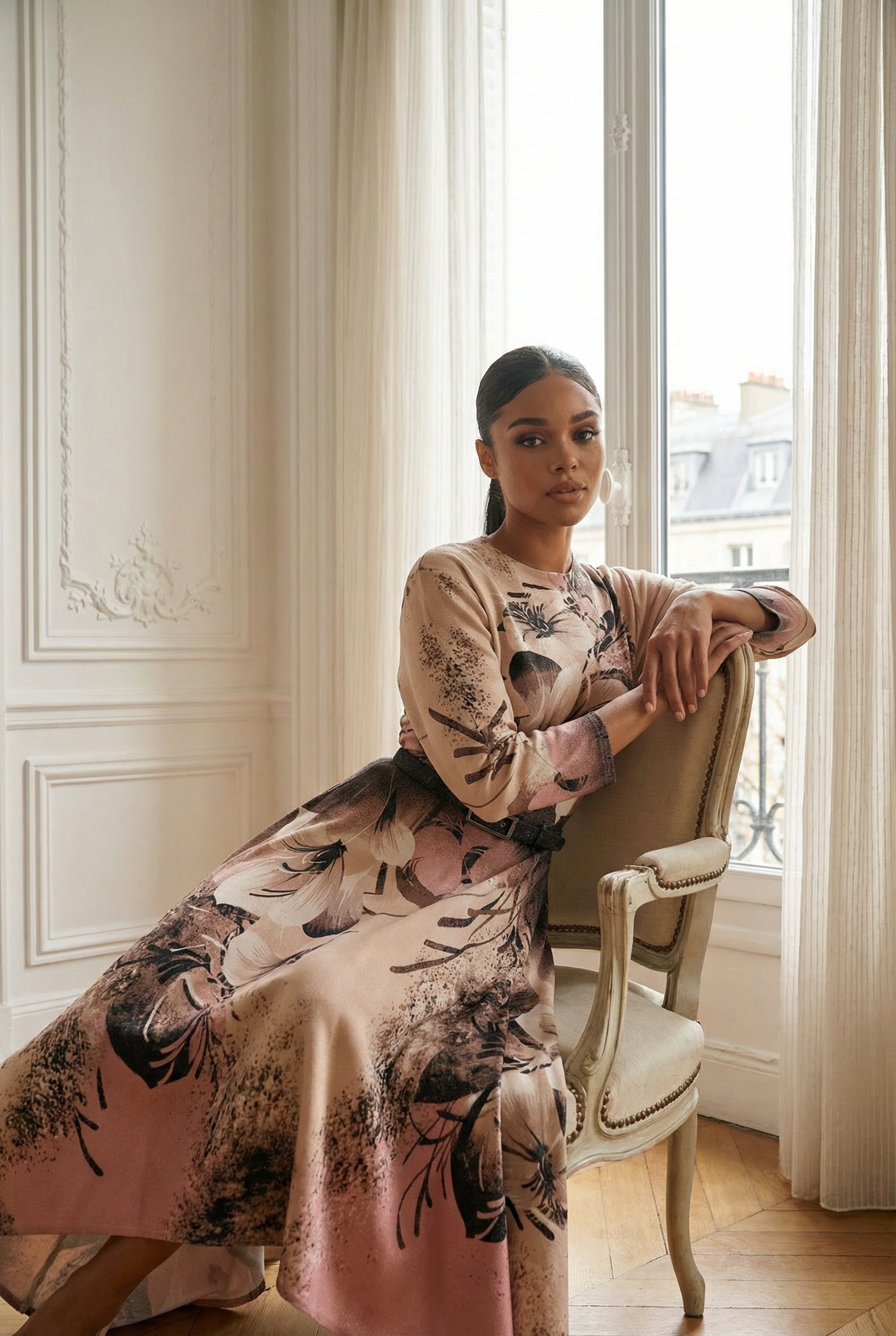 Woman in a floral dress sitting on a chair in a room with white walls and large windows.