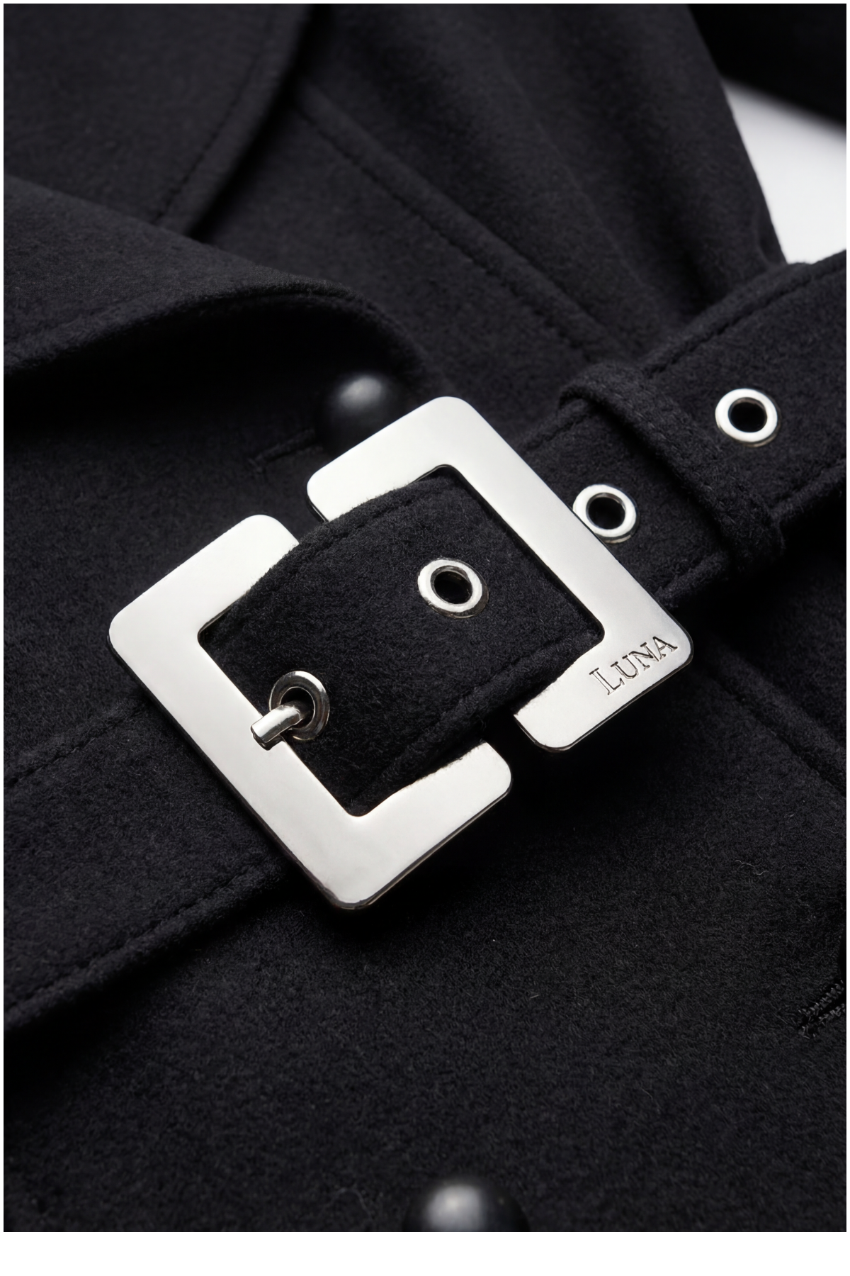 Close-up of a black coat with a silver belt buckle featuring the brand 'LUNA'.