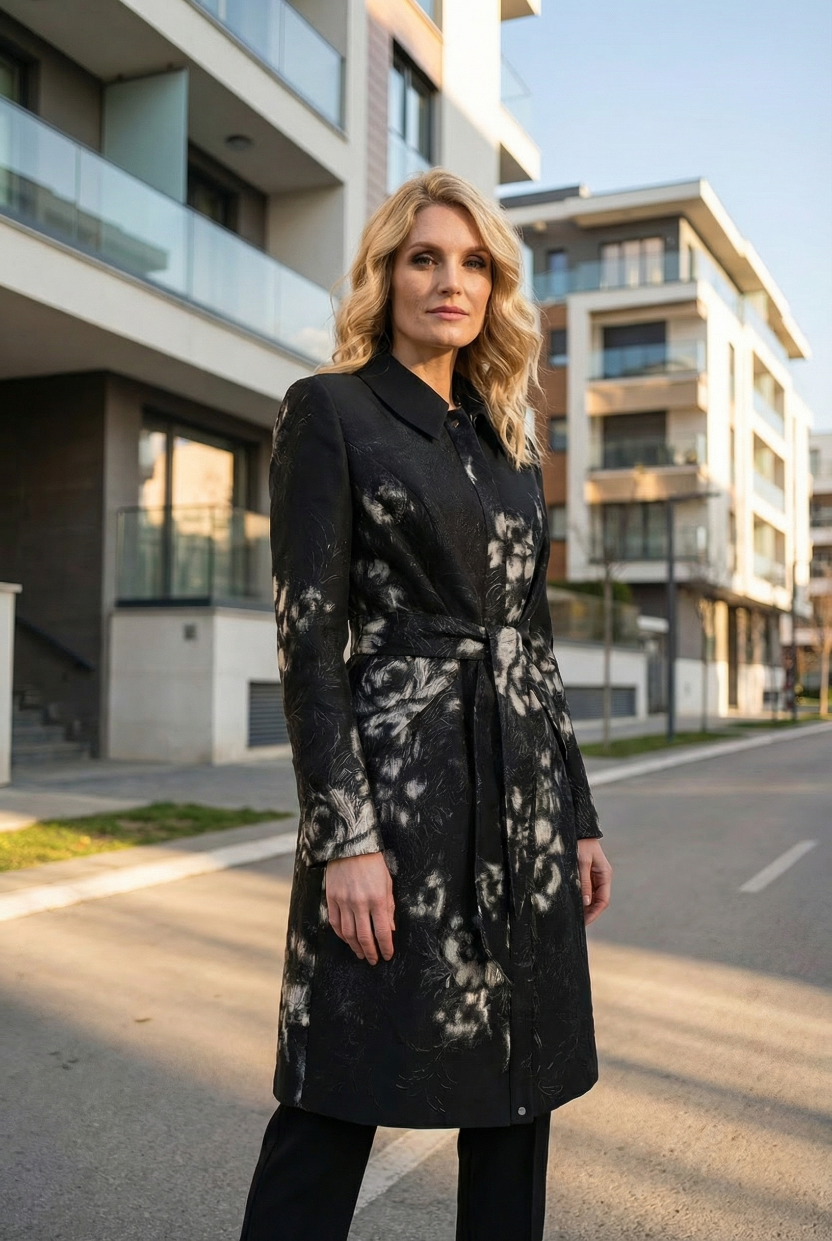 Woman wearing a black coat with a floral pattern standing on a street.