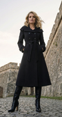 Woman wearing a black coat standing in front of stone walls.