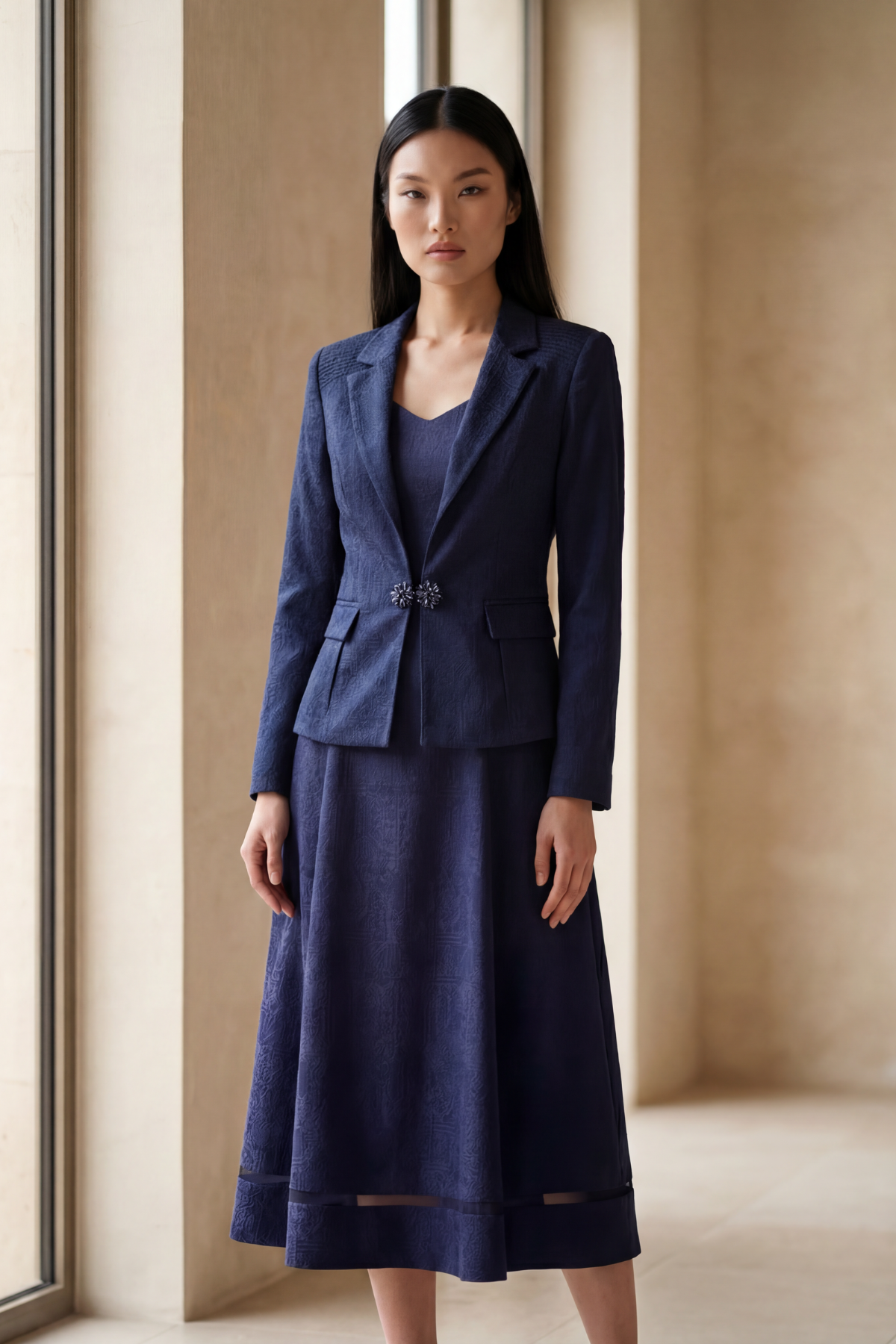 Woman wearing a blue suit standing in a room with large windows.