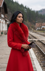 Red Wool Coat with Fur Collar, Lucy. Wool coat. Worn buttoned with the collar on, holding brown gloves on a railway platform.