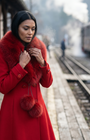 Red Wool Coat with Fur Collar, Lucy. Wool coat. Collar held closed at the neck on a railway platform, steam train behind.