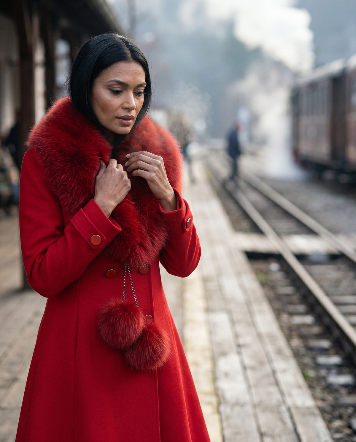 Red Wool Coat with Fur Collar, Lucy. Wool coat. Collar held closed at the neck on a railway platform, steam train behind.