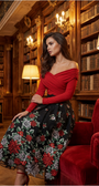 Woman in a red top and floral skirt sitting in a library.